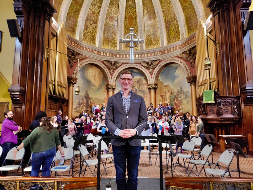 Dominick Diorio poses for a photo. Behind him are members of the Mendelssohn Choir