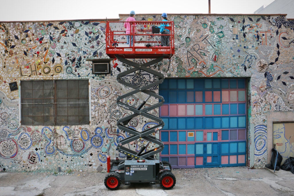 Andrew Jeffries and Stacey Holder stand on a scissor lift as they work on chiseling away important pieces to be salvaged from the mosaic at the Painted Bride Art Center