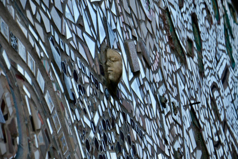 A tile bearing a double-sided face protrudes from a mosaic-ed wall.