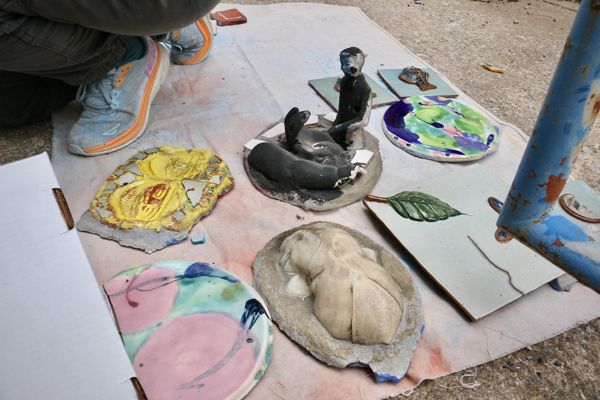 Sculptures and pieces of a mural lie on a piece of canvas on the ground.