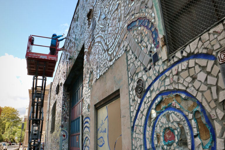 Andrew Jeffries and Stacey Holder stand on a lift, chiseling pieces from a mural on a building.