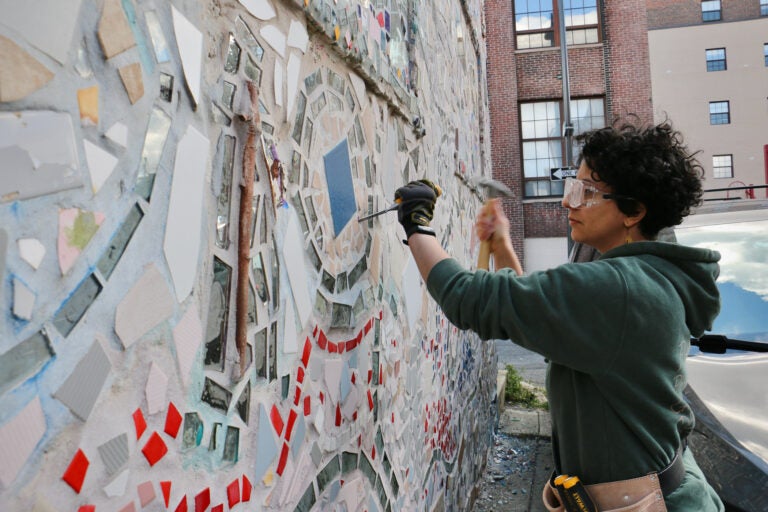 Preservation assistant Yaara Ben-Dor chisels a tile out of the facade of the Painted Bride Art Center
