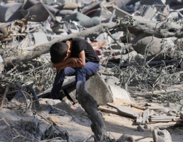 A Palestinian boy sits on the rubble of the building destroyed in an Israeli airstrike in Bureij refugee camp Gaza Strip, Wednesday, Oct. 18, 2023. (AP Photo/Hatem Moussa)