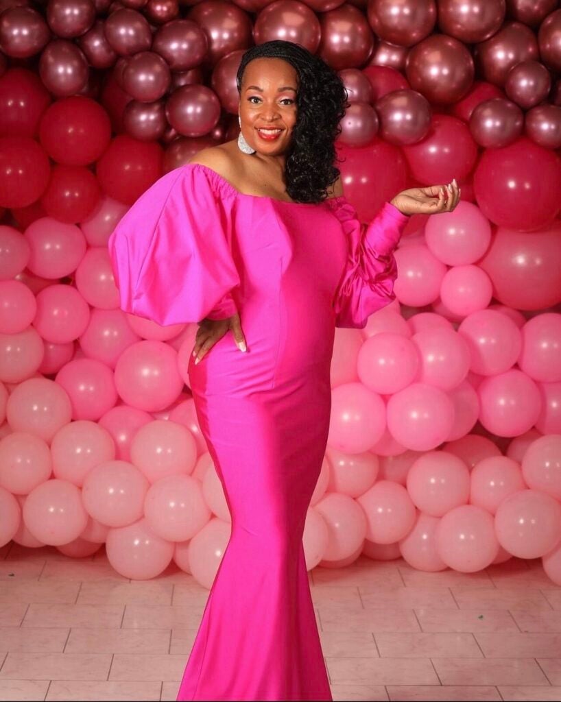 Traci Smith poses for a photo in a pink gown, with pink balloons in the background.