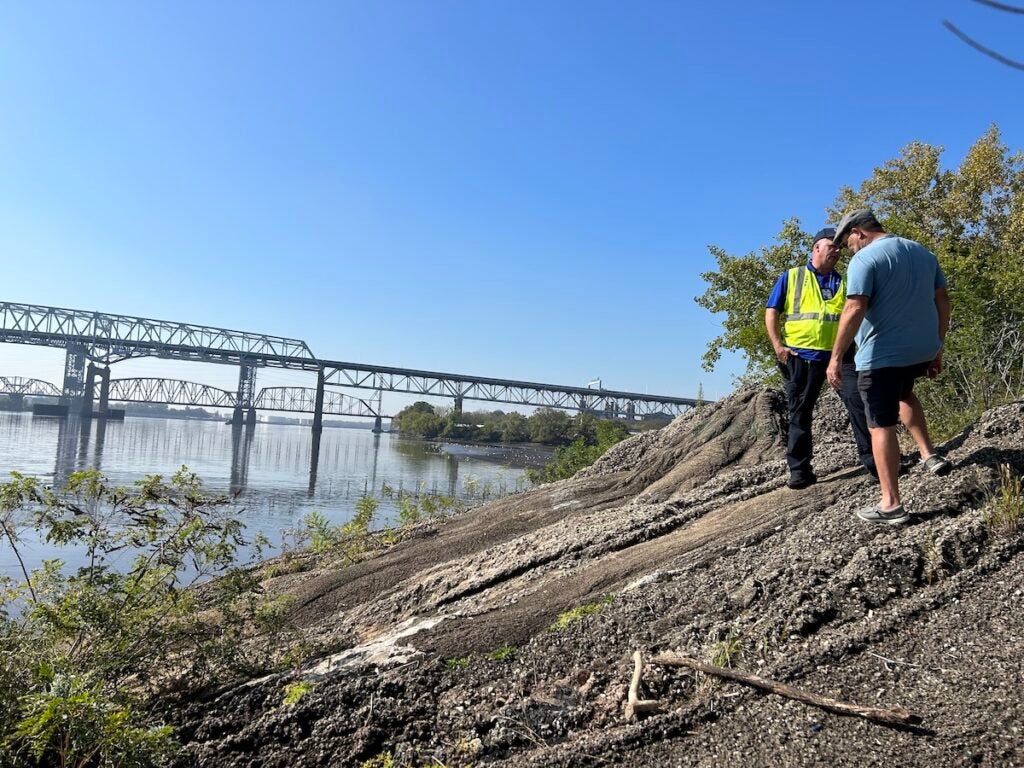 People stand on a hill of concrete. Beyond them is the Delaware River and a bridge.