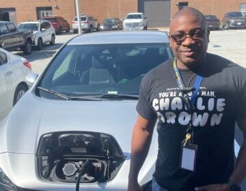 Chris Langhorn poses for a photo in front of his electric vehicle while it's charging.