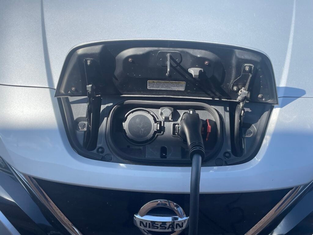 An EV charging cable connects to an outlet under the hood of a Nissan Leaf