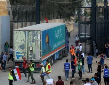 People on the Egyptian side of the Rafah border crossing watch as a convoy of lorries carrying humanitarian aid crosses to the Gaza Strip on Sunday.(Mohammed Assad/AFP via Getty Images)