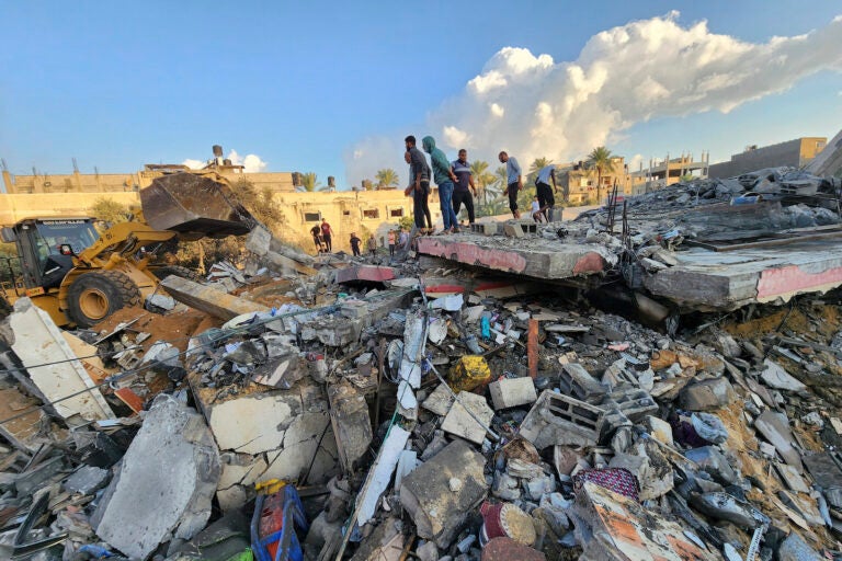 Palestinians stand by the rubble of a building destroyed in Israeli airstrikes in Deir el-Balah Gaza Strip