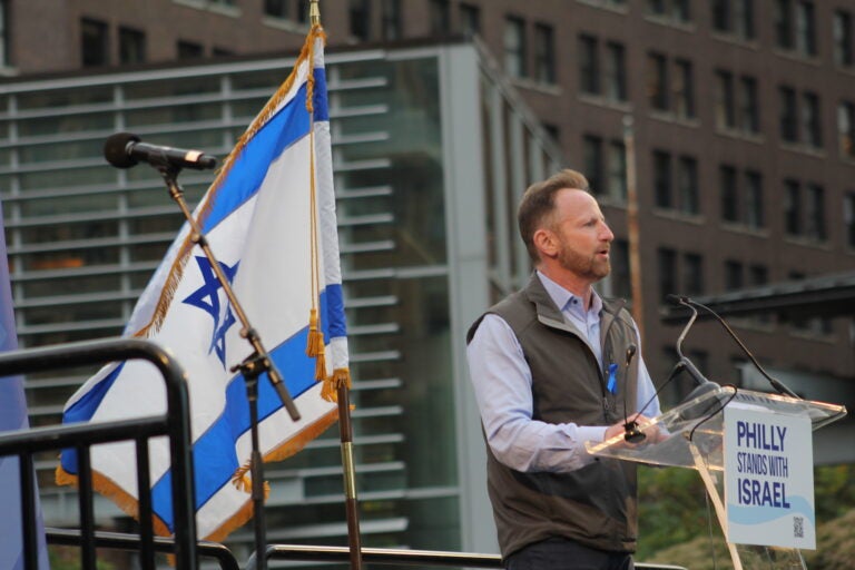 Michael Markman speaks at a podium with an Israel flag behind him