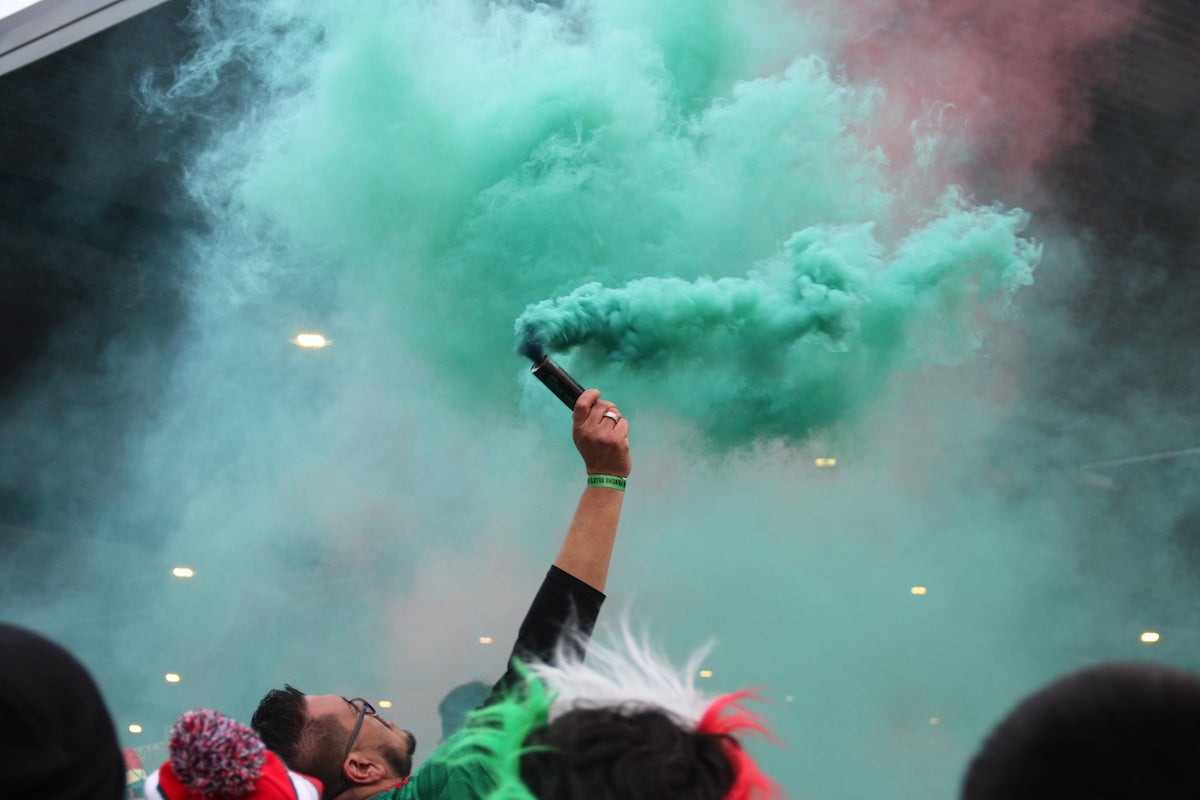 A fan releases a stream of green smoke, cheering for the Mexican national soccer team