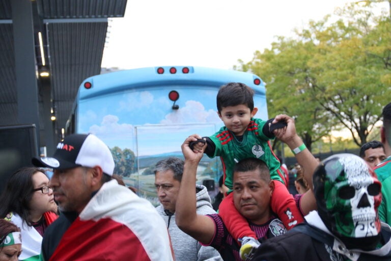 A young fan of Mexico's national soccer team sits on his caregiver's shoulders.