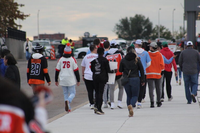 Fans wearing Phillies gear and Flyers gear walk down the sidewalk.