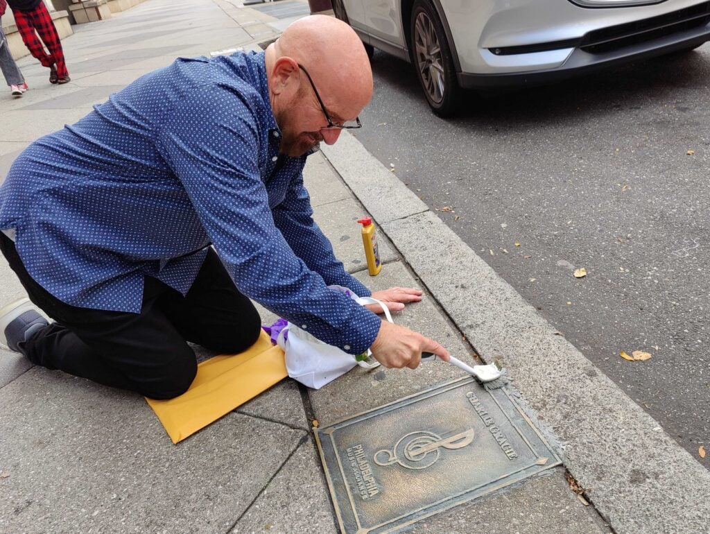 Charlie Gracie Jr. on his hands and knees scrubbing the sidewalk plaque.