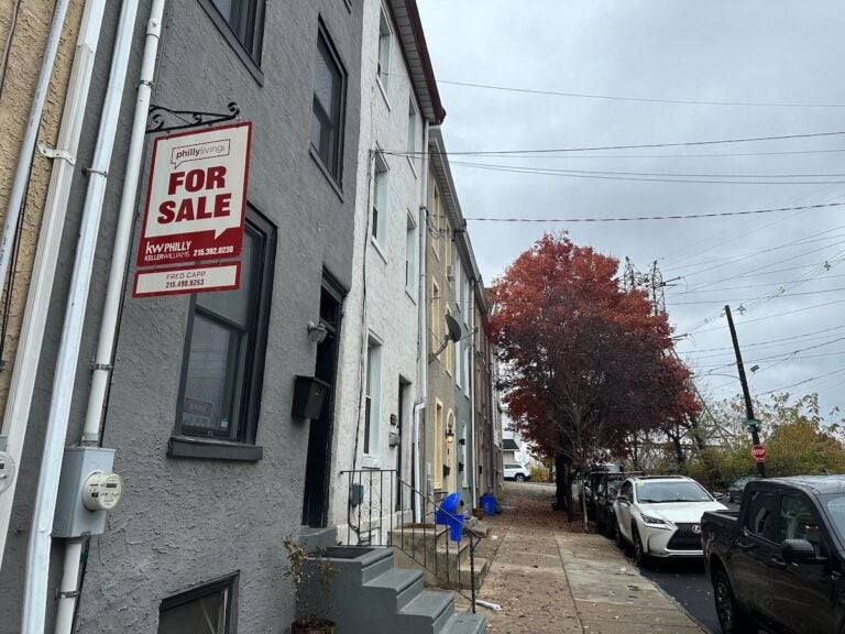 A for sale sign hangs outside of a rowhome