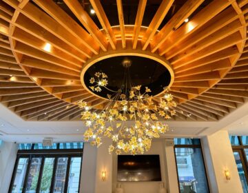 A golden chandelier and elaborate designs are visible on the ceiling of a large room.