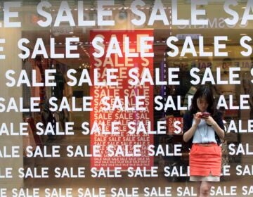 A person stands in front of a window with the word Sale plastered all over it.