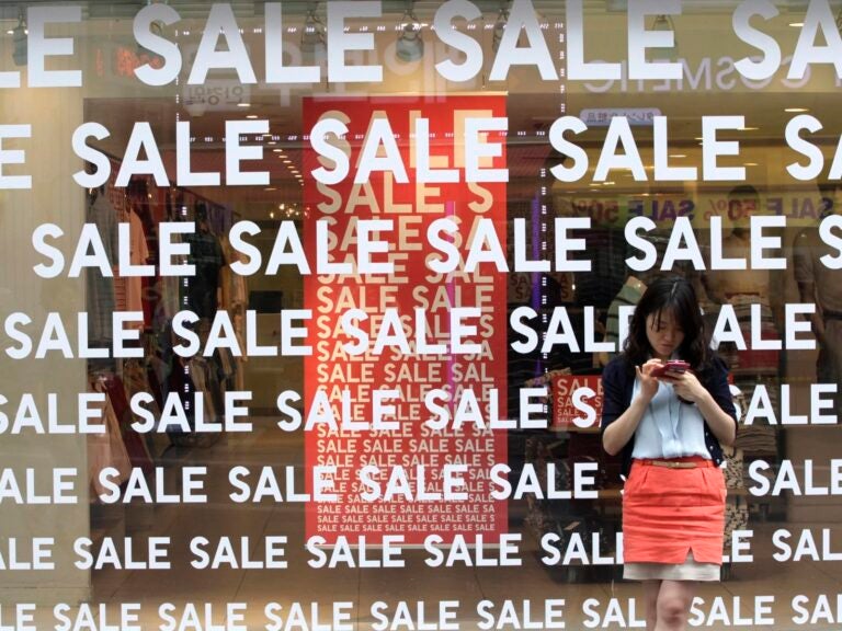A person stands in front of a window with the word Sale plastered all over it.