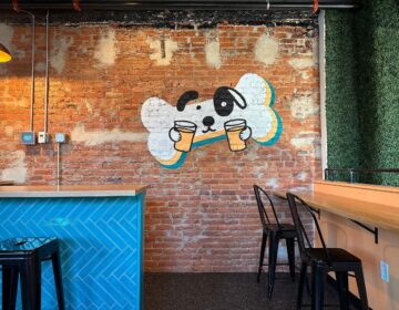 An image of a dog's face on a dog biscuit holding a couple of beers is painted on a brick wall behind a bar