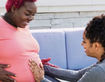 A doula places their hands on a pregnant person's stomach.