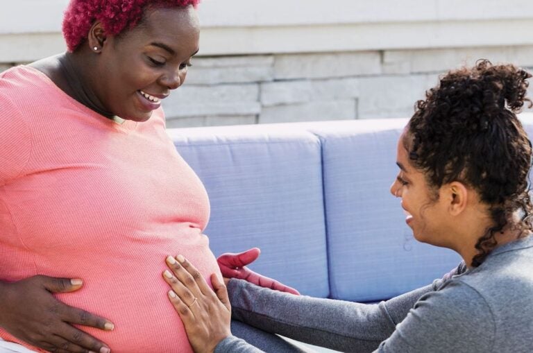 A doula places their hands on a pregnant person's stomach.