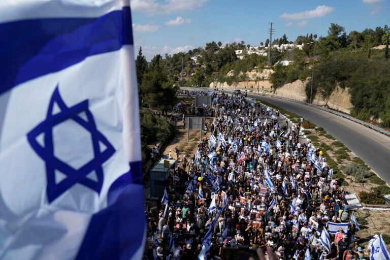 A flag of Israel is visible, and stretching into the distance is a crowd of people marching