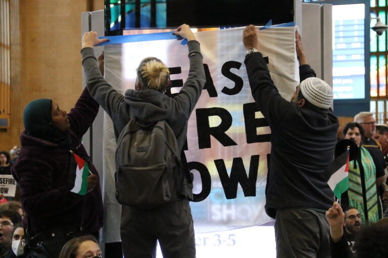 Protesters hang up a sign that reads Ceasefire now.