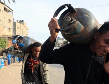 Men carry empty canisters to be filled with cooking gas from a tanker