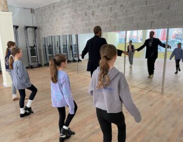 Kids face towards their teachers as the teacher demonstrates a certain tap dance step