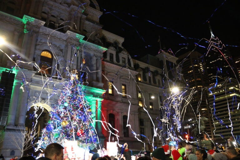 Confetti flies through the air. In the background is Philadelphia's holiday tree and City Hall