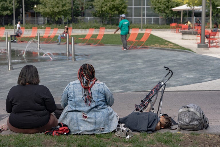 2 woman with a young child sitting on the ground in the park.