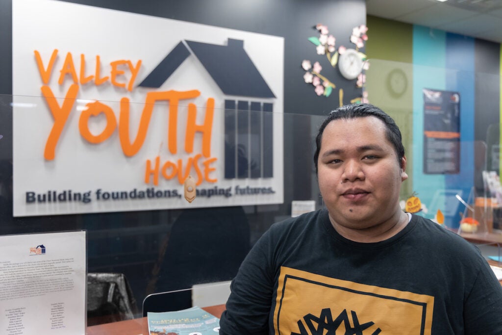 Paulo Garcia poses for a photo in front of a sign that reads Valley Youth House