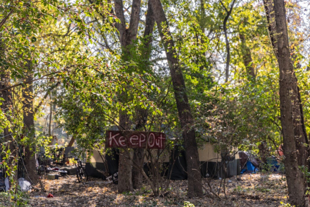 A sign says 'Keep Out' at the encampment in the woods