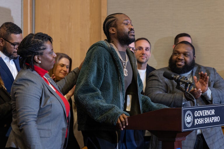 Joanna McClinton stands next to Meek Mill as he speaks into a microphone at a podium