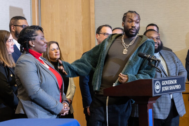 Meek Mill speaks into a microphone at a podium surrounded by lawmakers