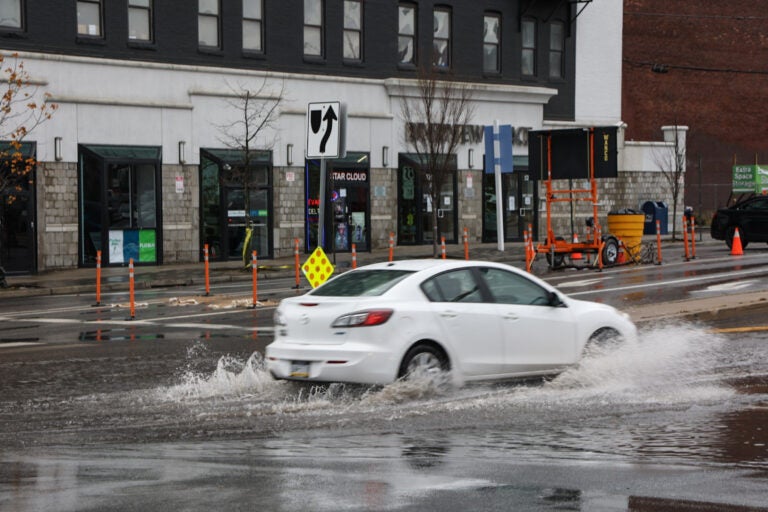 Cars drove through standing water onto Spring Garden Street in Philadelphia after a storm brought heavy rain to the region and the Delaware River overflowed onto the road on December 18, 2023. (Kimberly Paynter/WHYY)