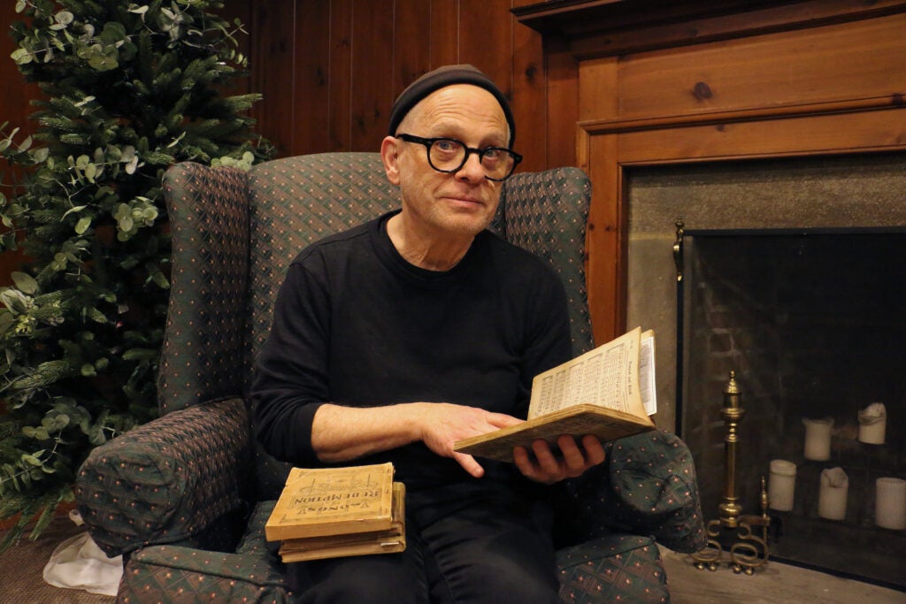 Composer David Lang poses for a photo, looking up, with a book in hand while seated in an armchair.