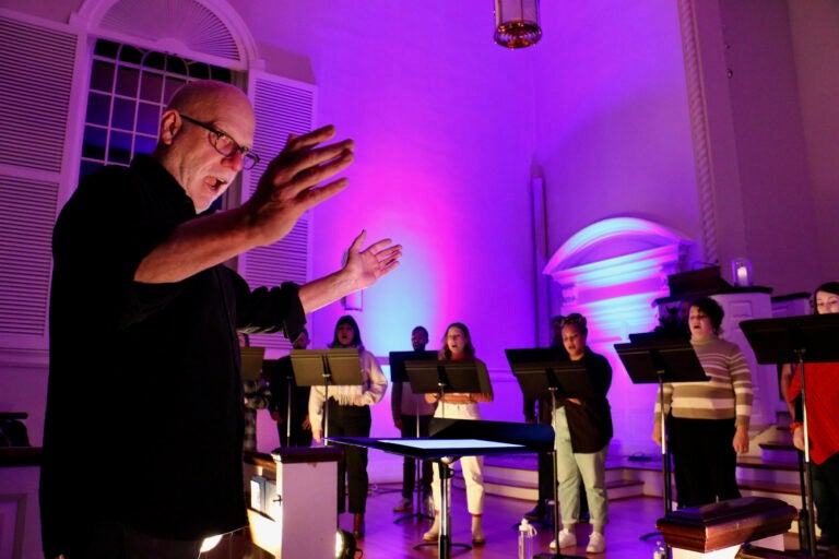 Donald Nally conducts in the foreground. In the background, members of The Crossing sing.