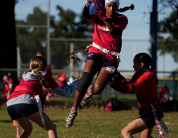 Sonya Chalil (center) jumps between, Kirby White (left) and Bella Franks (right) during practice with Texas Fury, an all-girls flag football select travel team,Sunday, Dec. 10, 2023, in Austin, Texas. Flag football's inclusion in the 2028 Summer Olympics in Los Angeles only enhances the profile of a sport that's growing by leaps and bounds on the women's side. (AP Photo/Eric Gay)