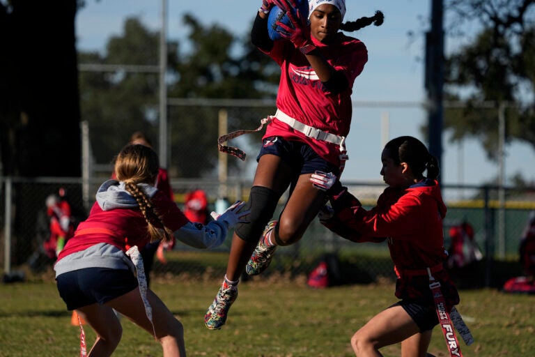 Sonya Chalil (center) jumps between, Kirby White (left) and Bella Franks (right) during practice with Texas Fury, an all-girls flag football select travel team,Sunday, Dec. 10, 2023, in Austin, Texas. Flag football's inclusion in the 2028 Summer Olympics in Los Angeles only enhances the profile of a sport that's growing by leaps and bounds on the women's side. (AP Photo/Eric Gay)