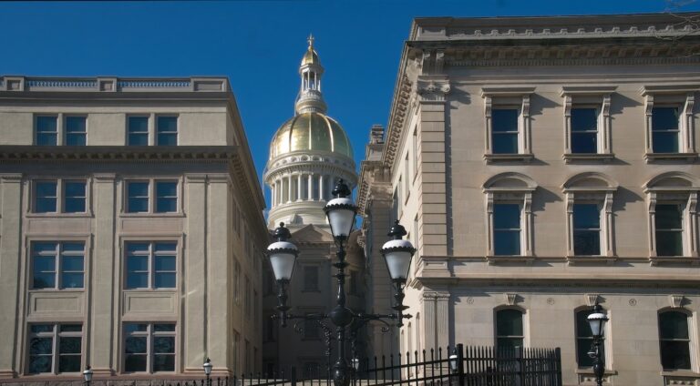 The New Jersey state capitol building dome as seen through a gap in several buildings.