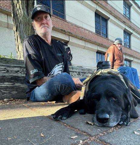 Breaking Bread resident Chuck Jones sits on the sidewalk with his emotional support and medical alert dog, Midnight.