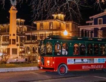 A trolley goes by Victorian homes lit up with lights