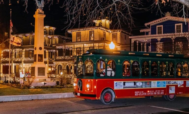 A trolley goes by Victorian homes lit up with lights