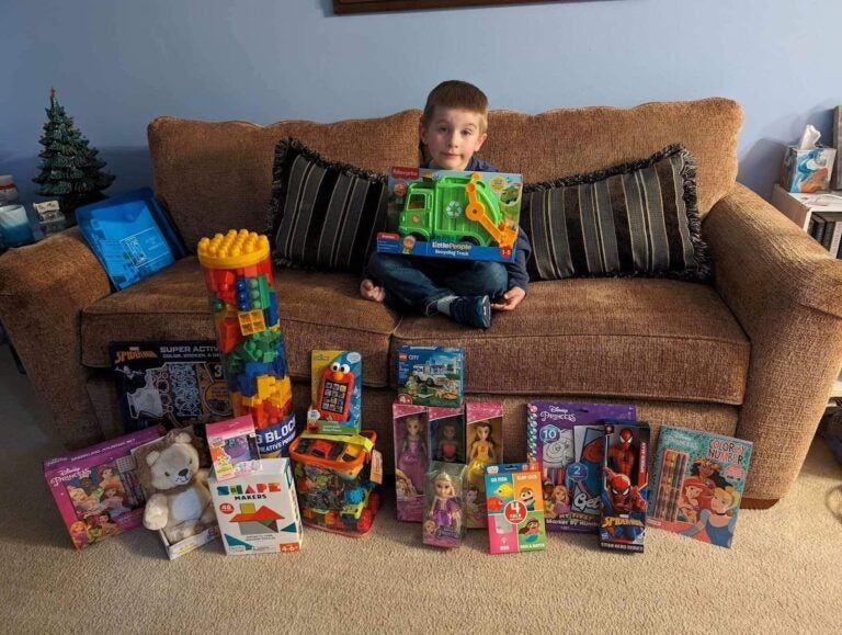 Colton White sits on a couch, posing for a photo surrounded by donated toys for the toy drive for Nemours Children's Hospital