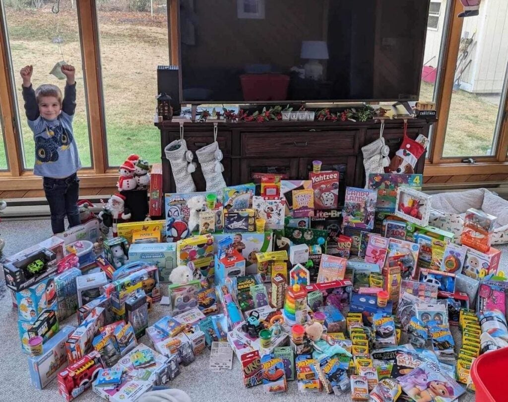 Colton White raises his arms up as he stands behind rows of donated toys