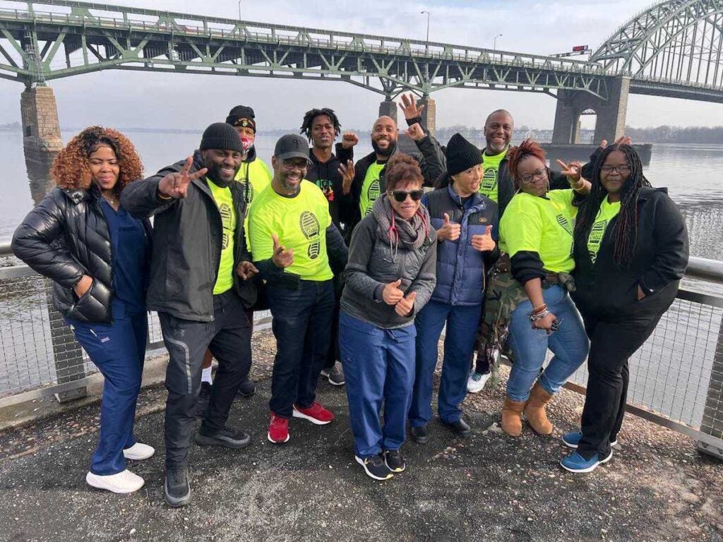 A group of people poses for a photo at a pier in front of the Benjamin Franklin Bridge.