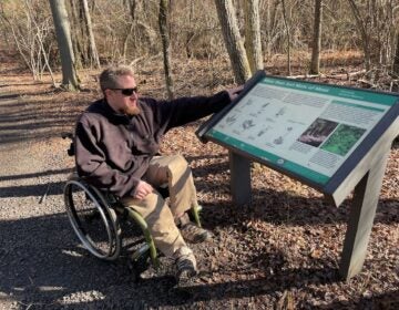Sean Holland, the Access Nature Disability Advocate for the Pinelands Preservation Alliance, points towards a sign on a trail.