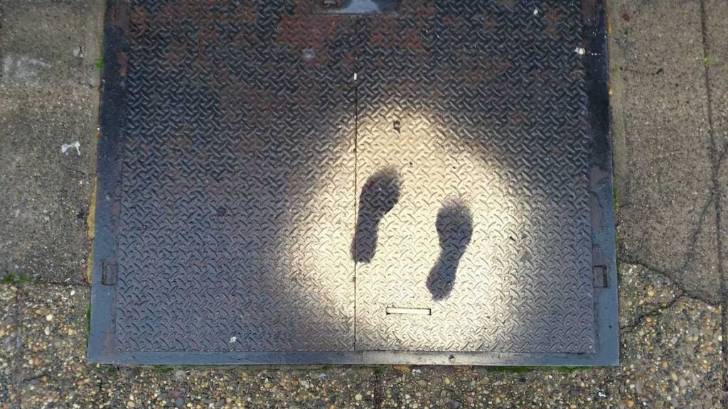 An outline of shoes on the sidewalk in gold spray paint