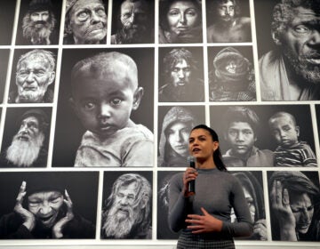 Leah den Bok speaks into a microphone in front of portraits she has made of people experiencing homelessness